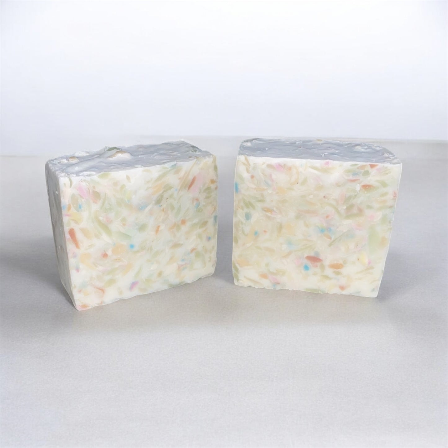 Two blocks of white soap with colorful specks on a light gray background