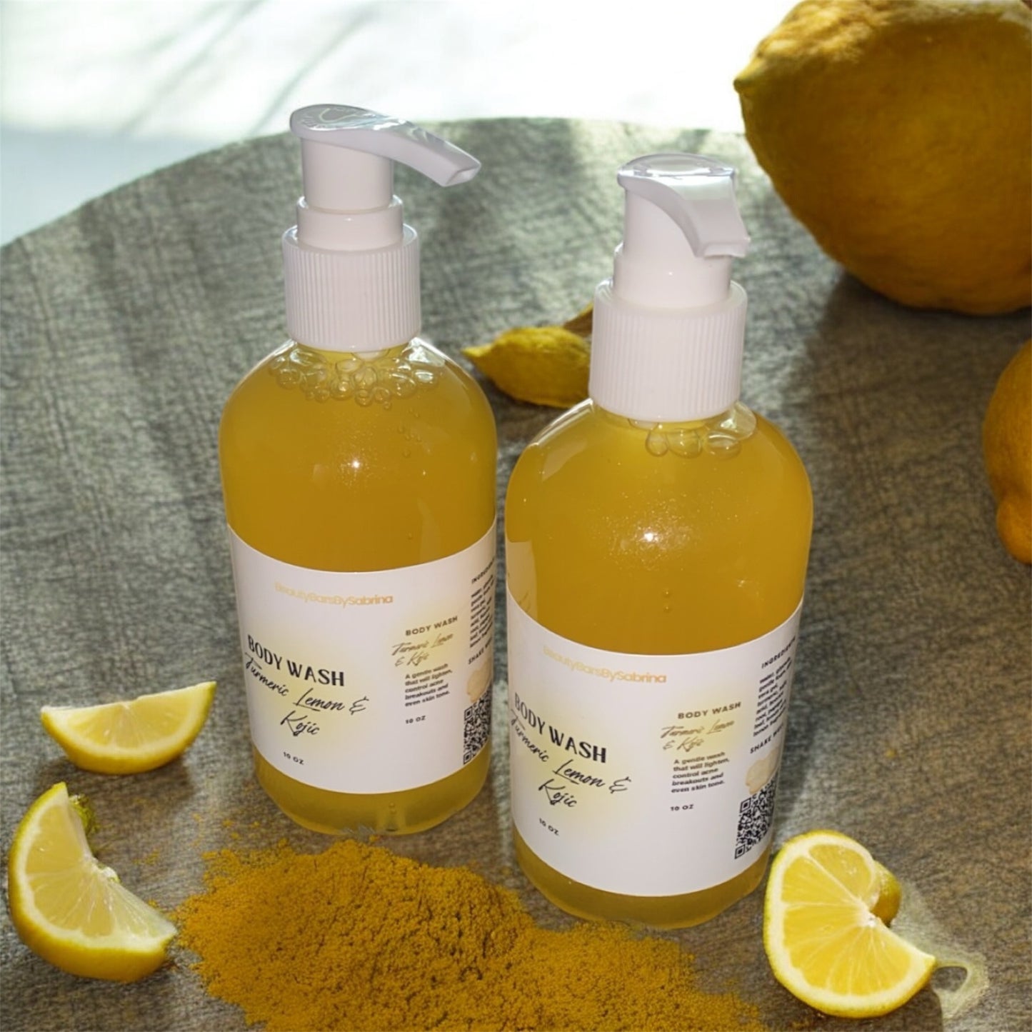 Two bottles of body wash with lemon and turmeric ingredients on a textured surface.