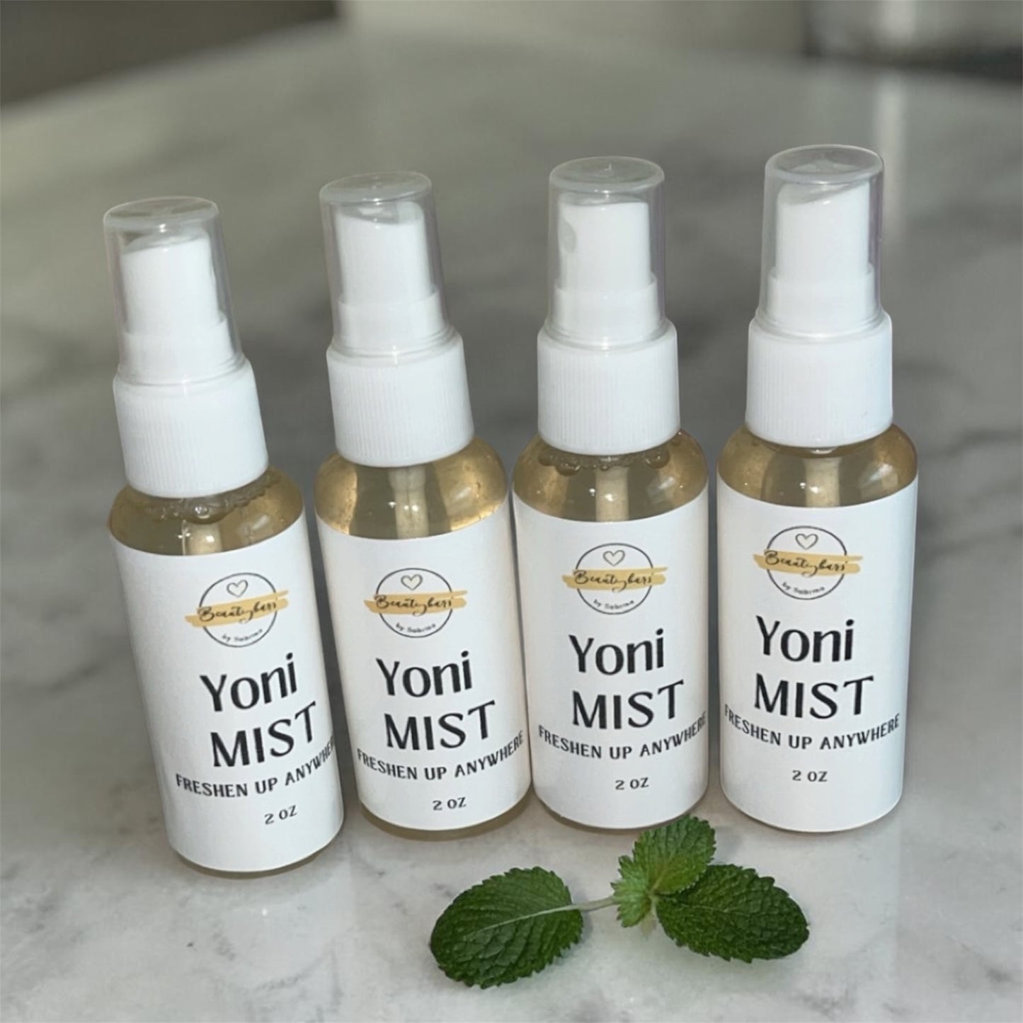 Four bottles of Yoni Mist on a marble surface with mint leaves.