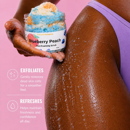 A person applies blueberry peach exfoliating scrub from Yoni Foaming Scrub onto their back. The person is wearing a purple sports bra, and the background is a solid pink color with text describing the benefits of the exfoliating scrub.