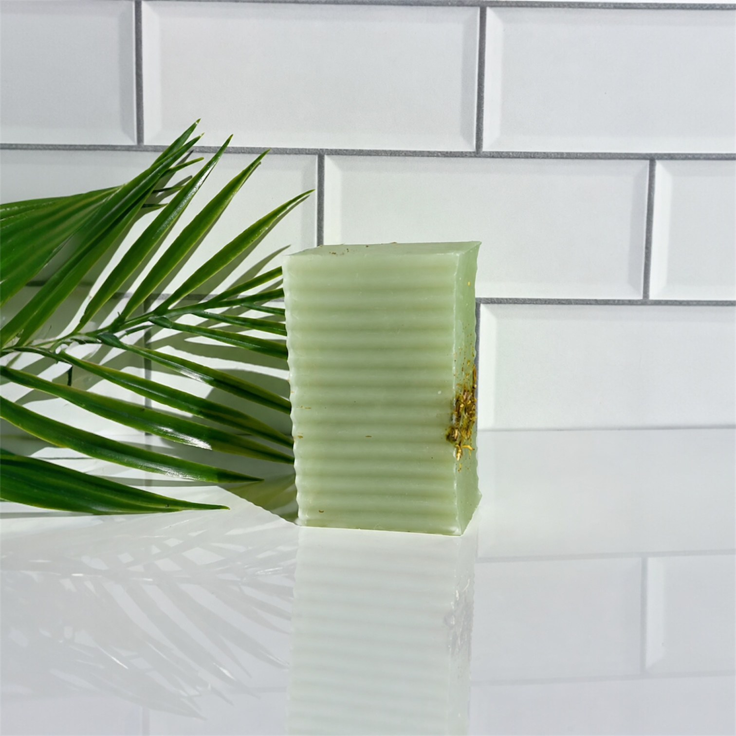 Green bar of soap on a white tiled surface with a leaf in the foreground
