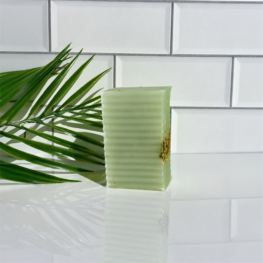 Green bar of soap on a white tiled surface with a leaf in the foreground