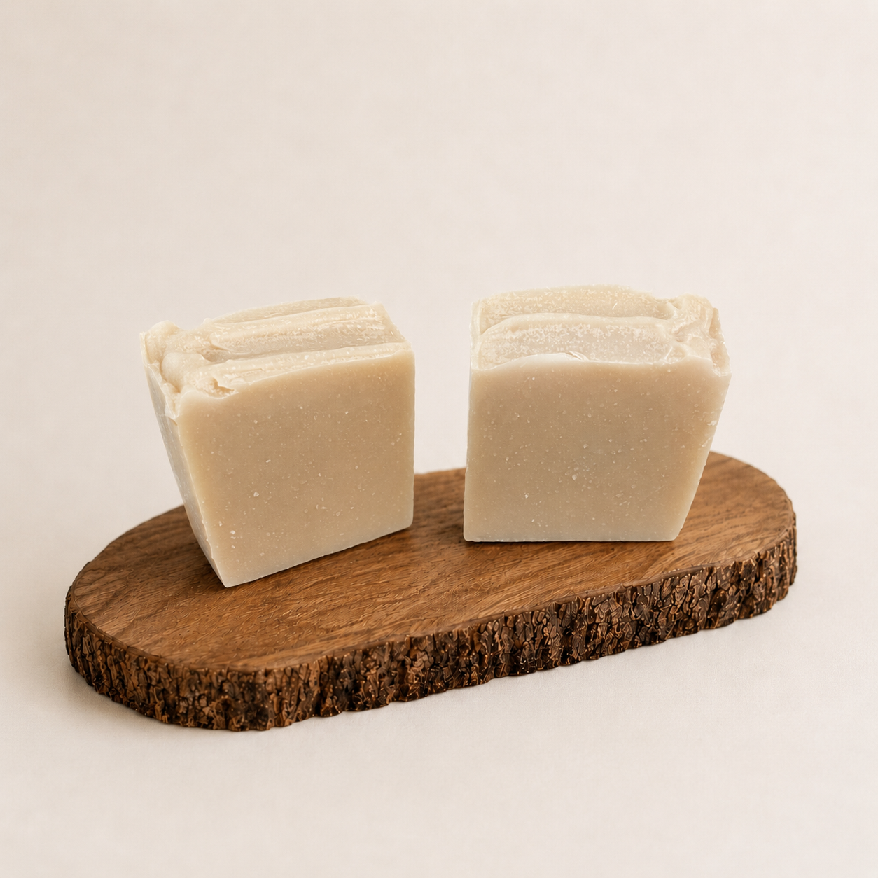 Two bars of soap on a wooden block with a plain background
