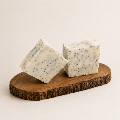 Two square-shaped soaps with cranberry seeds specks on a wooden board against a light background