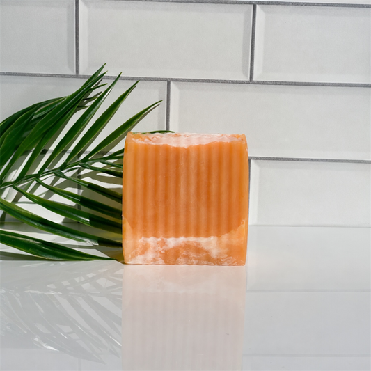 Orange soap bar on a white surface with a green leaf and tiled wall background