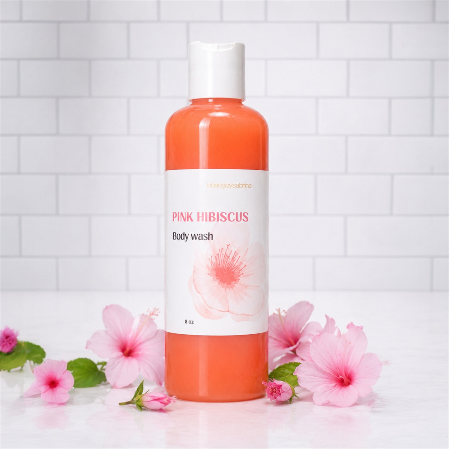 Bottle of Pink Hibiscus body wash with flowers on a white tiled background