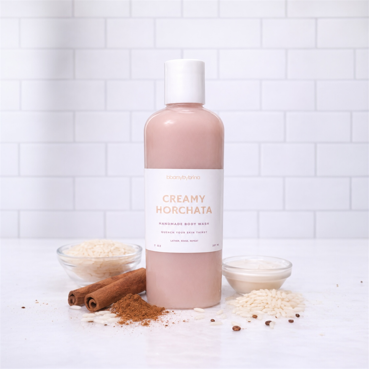 Bottle of 'Creamy Horchata' body wash with cinnamon sticks and rice on a white tiled background
