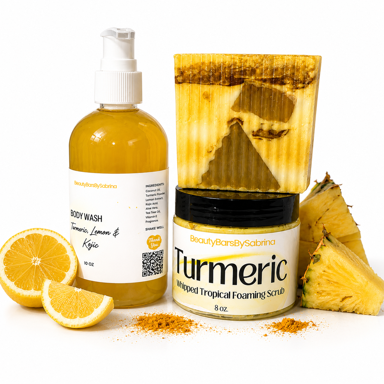 Beauty Bars by Sabrina body care set featuring a Turmeric Lemon & Kylic body wash bottle, a jar of Turmeric whipped tropical foaming scrub, a bar of honey-colored soap, and fresh pineapple and lemon slices on a white background.