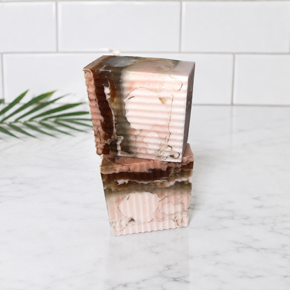 Two stacked rectangular bars of handmade soap with a pink, brown, and white marble pattern, set on a white marble countertop with a white subway tile backsplash.