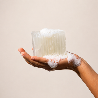 Hand holding a soap with suds against a plain background