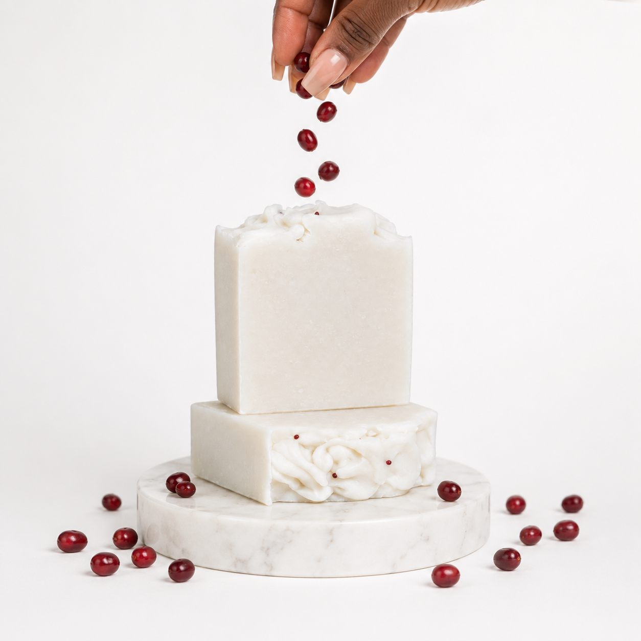 White soap bars with red berries on a marble stand against a white background
