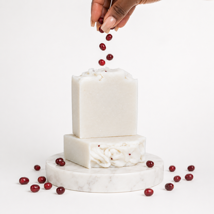 White soap bars with red berries on a marble stand against a white background