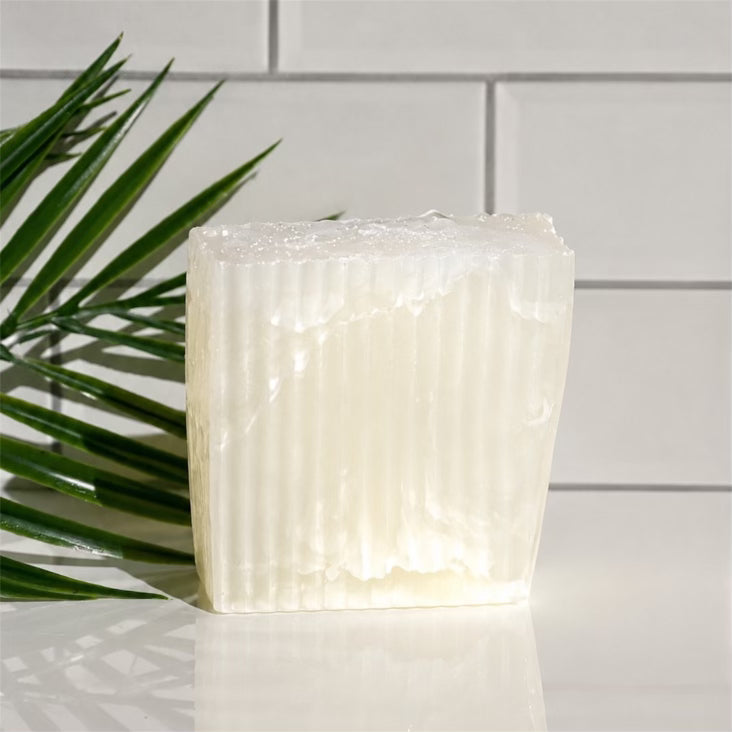 Textured white soap on a reflective surface with a plant leaf and tiled wall background