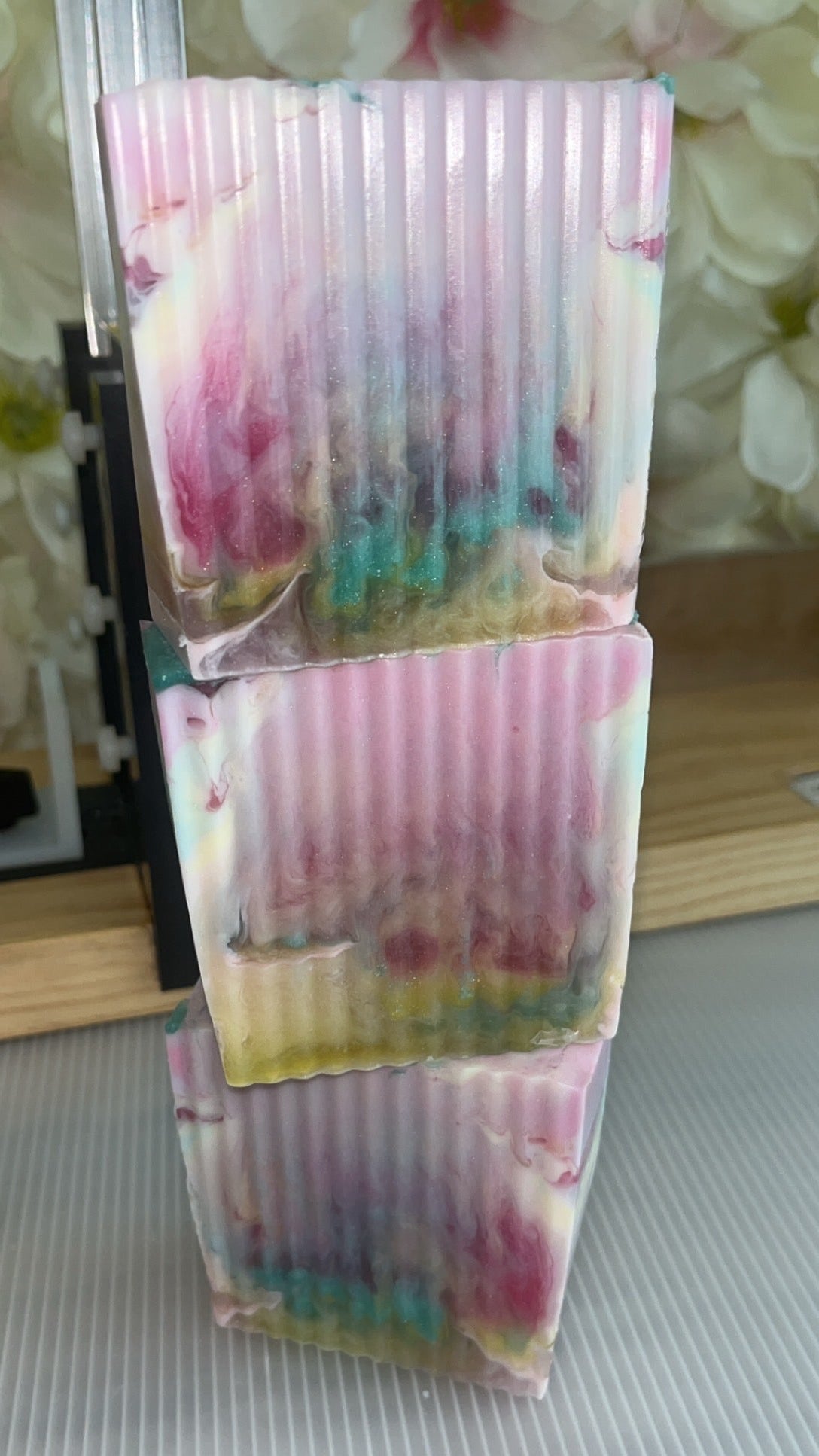 Stack of colorful soaps with a floral pattern on a textured surface.