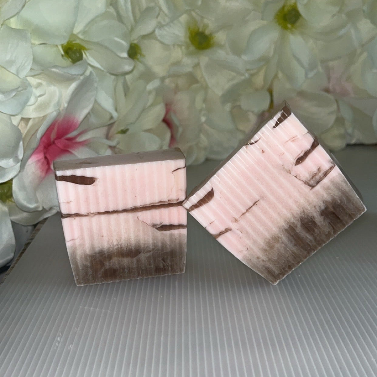 Pair of pink and brown soaps on a textured surface with a floral background