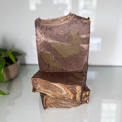 Two stacked soap bars with a natural, mottled brown and green pattern on a white surface.