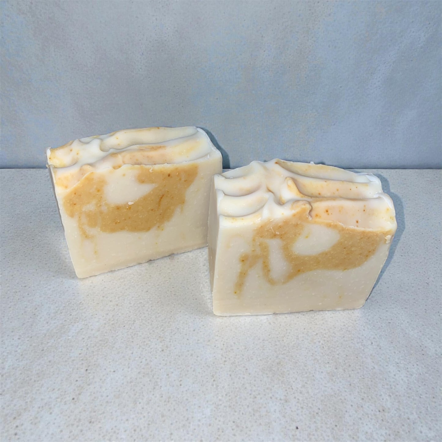 Two marbled soap bars on a textured surface with a light gray background