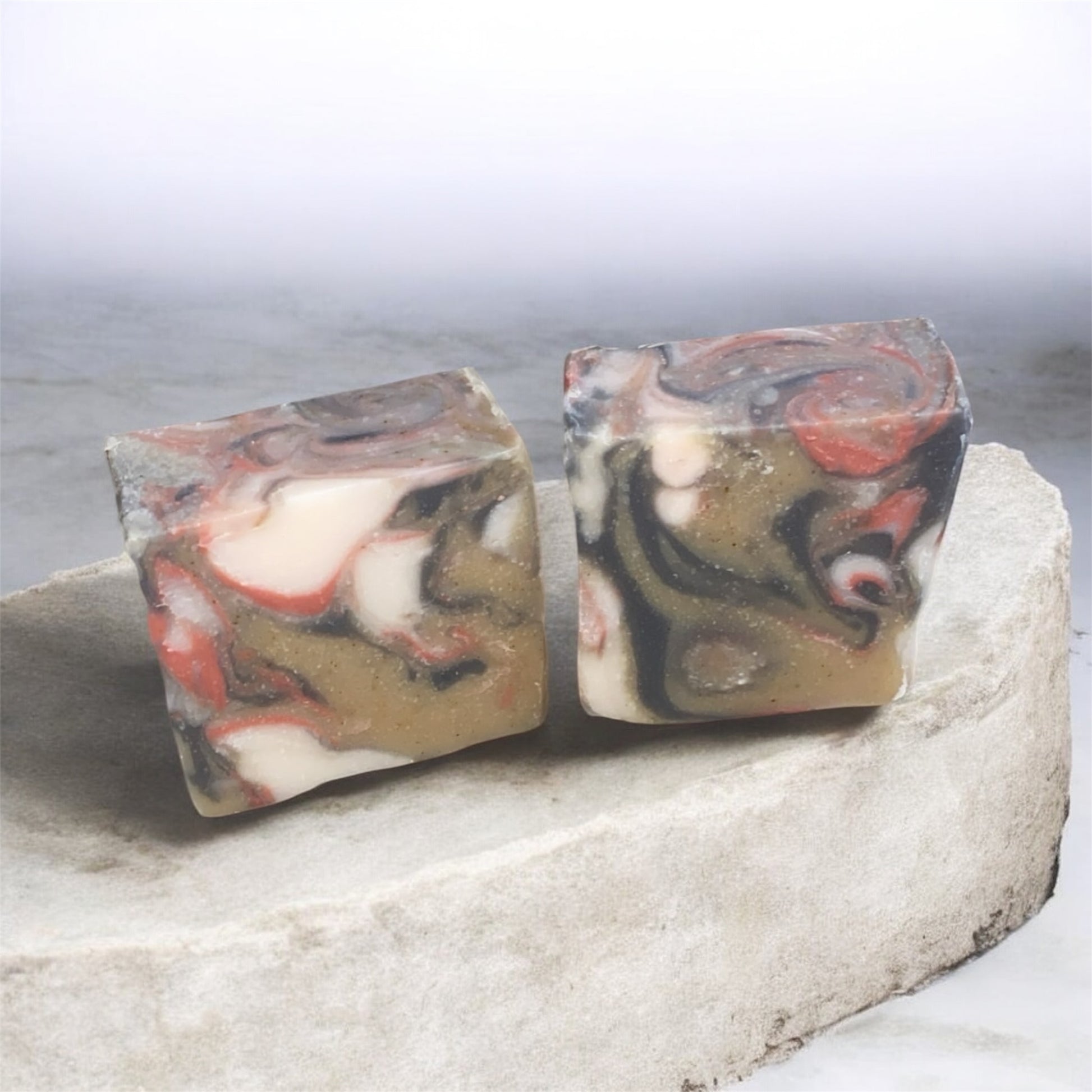 Two marbled soap bars on a stone surface with a light gray background