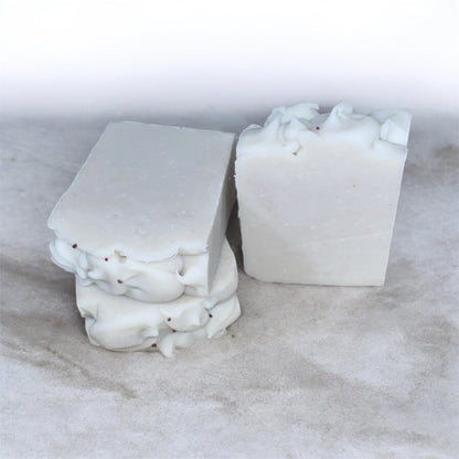 Two white soap bars with red cranberry seeds on top and  on a marble surface