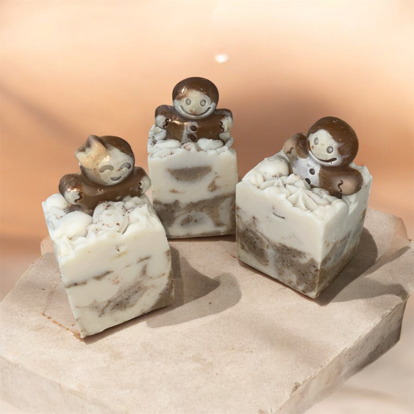 3 small soap with a gingerbread man figures on top with marbled design on a beige background