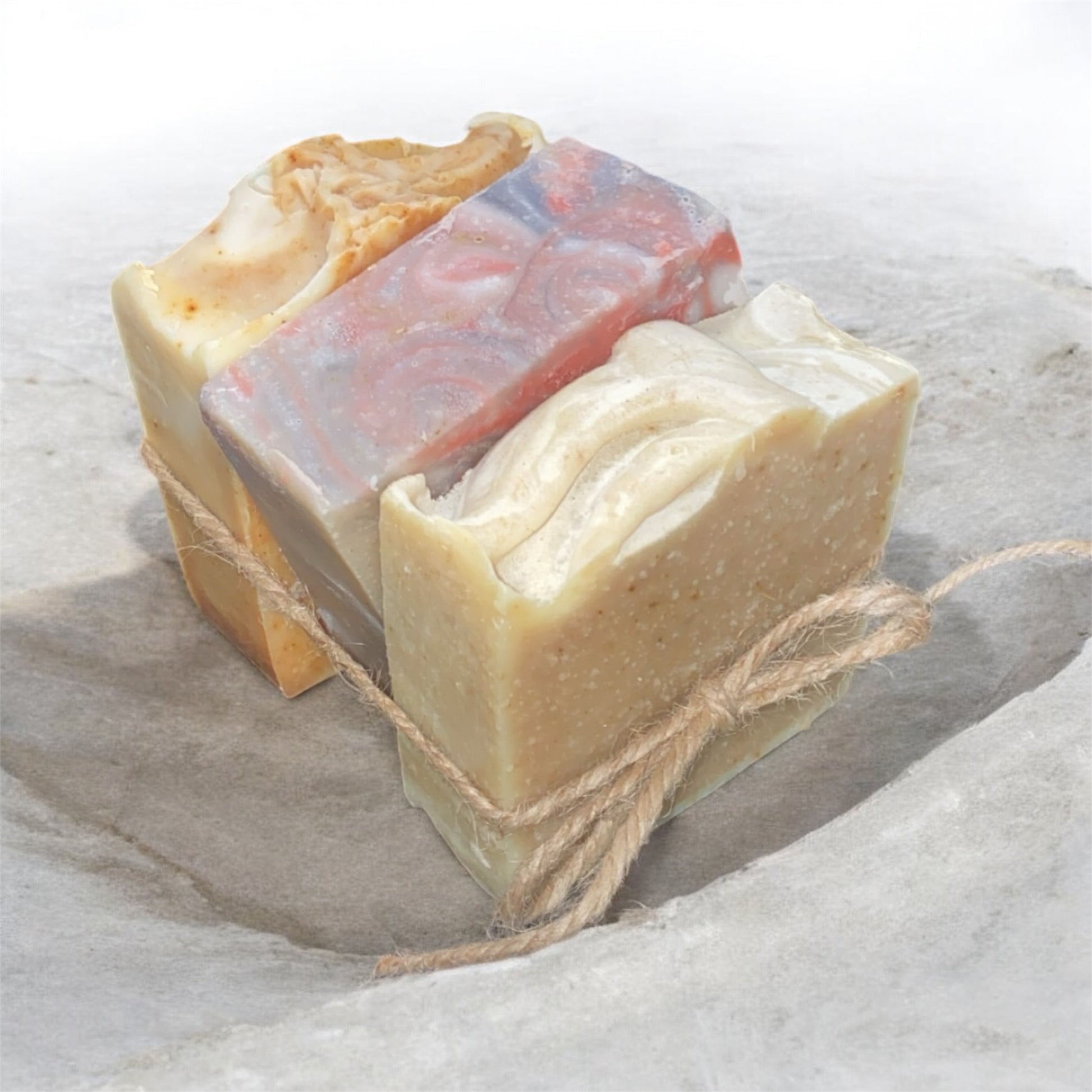 Three bars of soap with different colors tied together with twine on a textured surface.