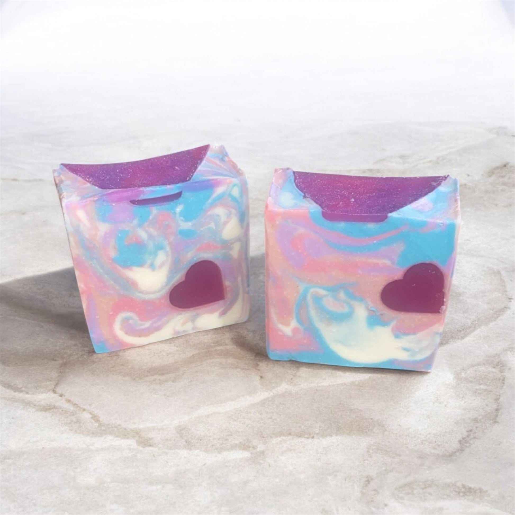 2 soaps with vibrant colors of purple,pink, white and blue with a heart embed with white and stoned background.