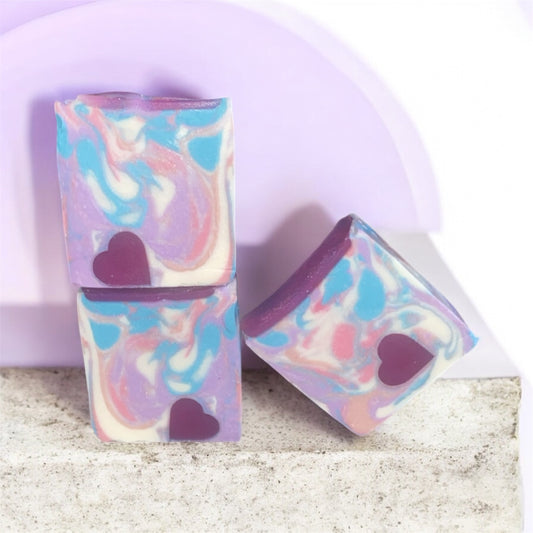 3 soaps with vibrant colors of purple,pink, white and blue with a heart embed with white and stoned background.