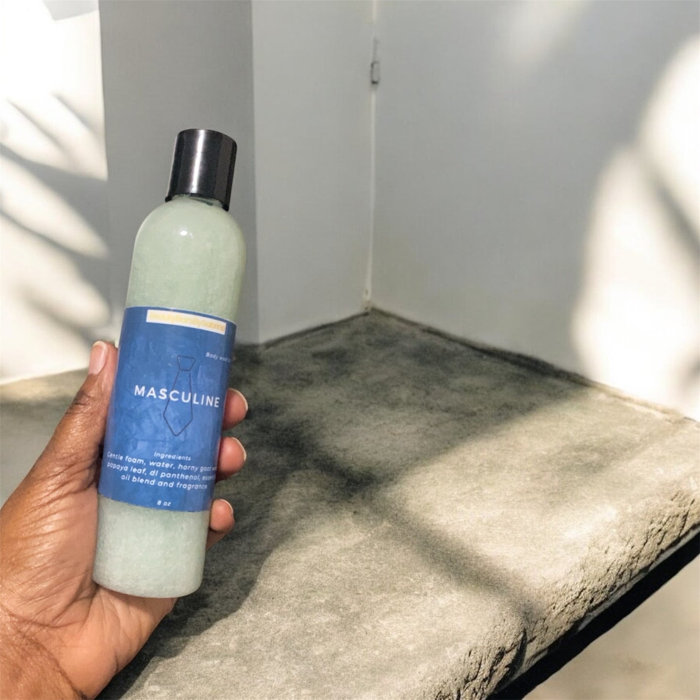 A bottle filled with body wash next to stone while someone holding bottle 