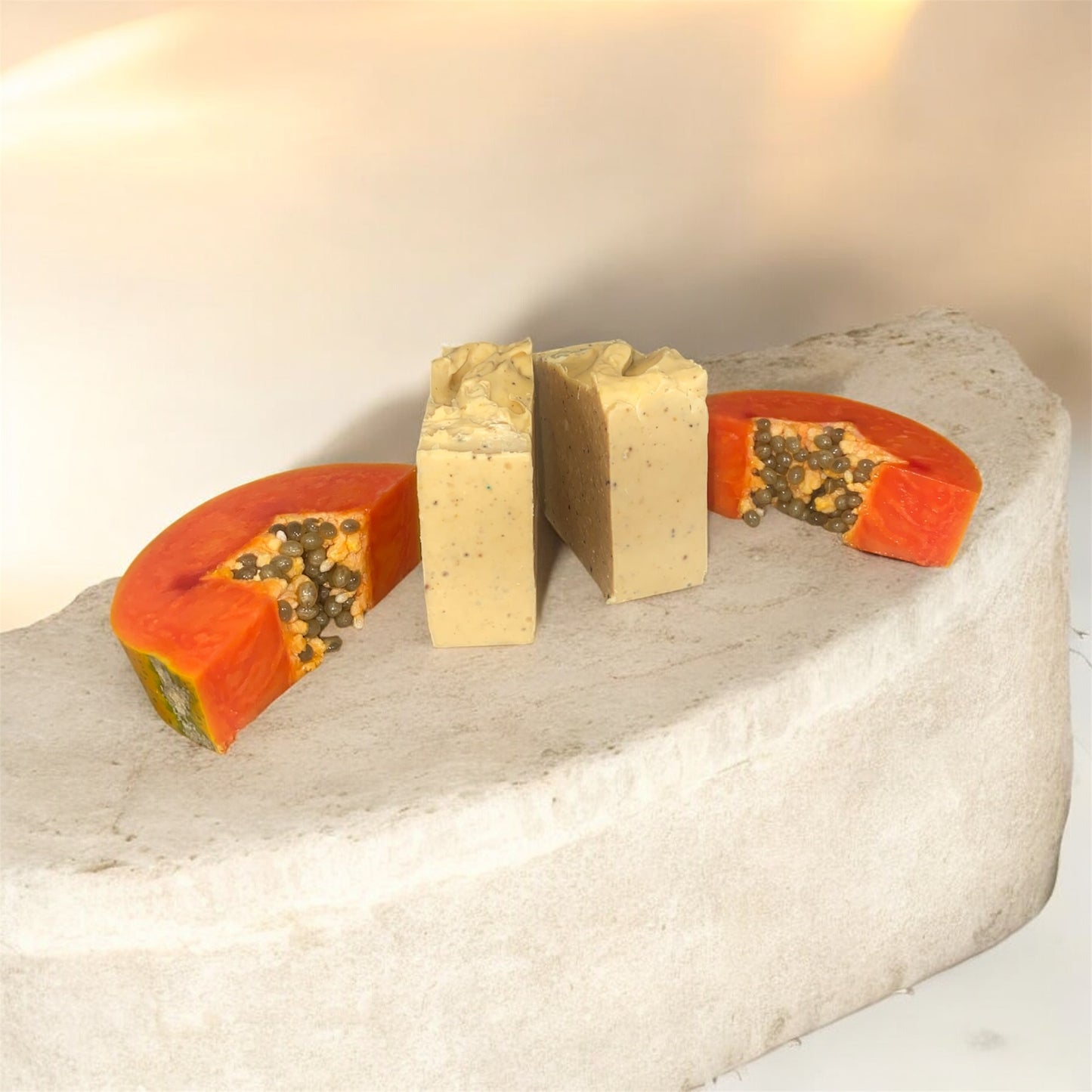 2 soap bars on rock with a papaya next to it displaying the soap.