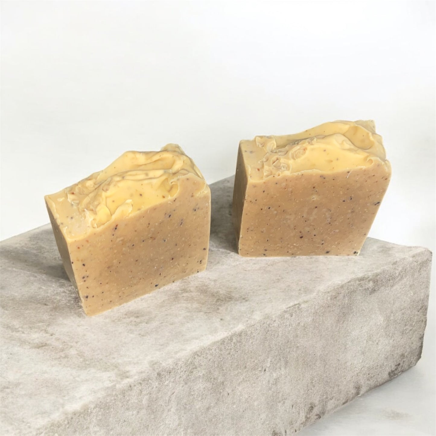 Two beige soap bars on a gray stone surface with a white background