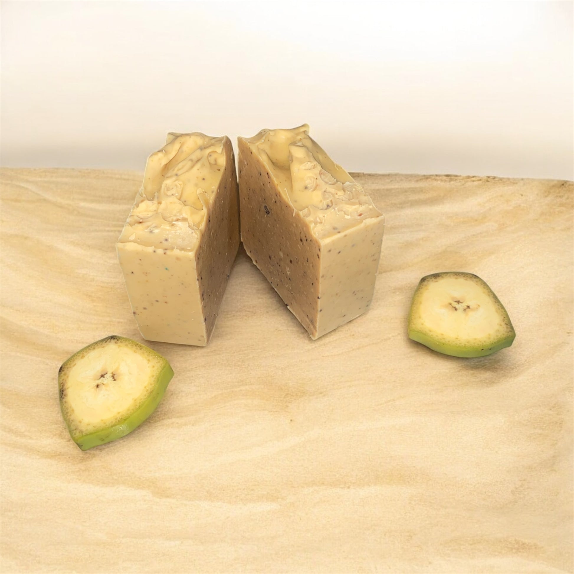 Two pieces of beige soap with green  plantain slices on a wooden surface