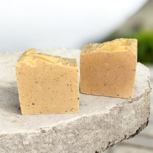 Two beige soap bars on a stone surface with a blurred natural background
