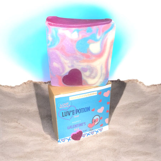 Colorful soap box with heart design on a box labeled 'Luv'e Potion' soap against a white backdrop background and colorful soap on top.