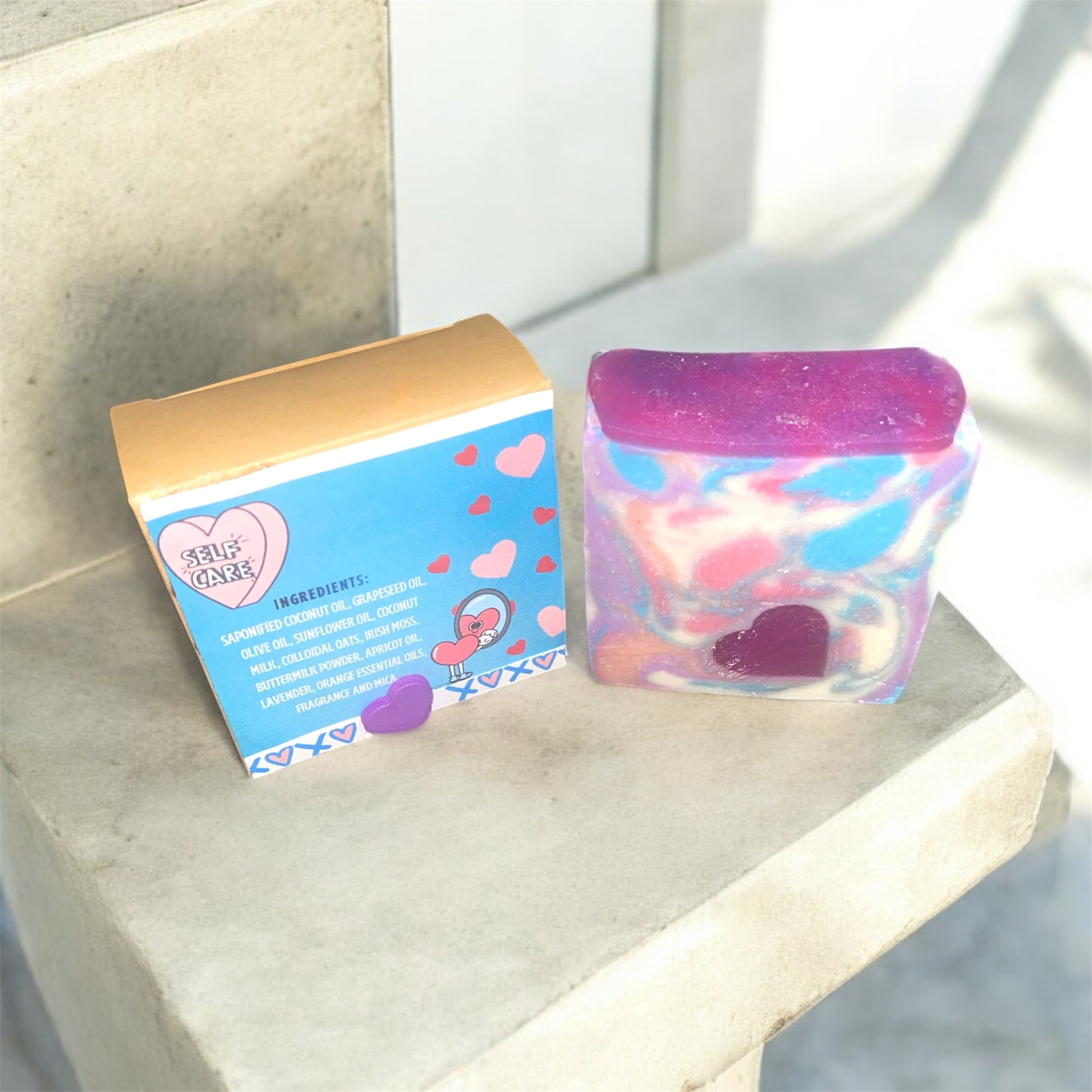 Colorful soap box with heart design on a box labeled soap against a white backdrop background and colorful soap next to it with ingredients showing on the box.