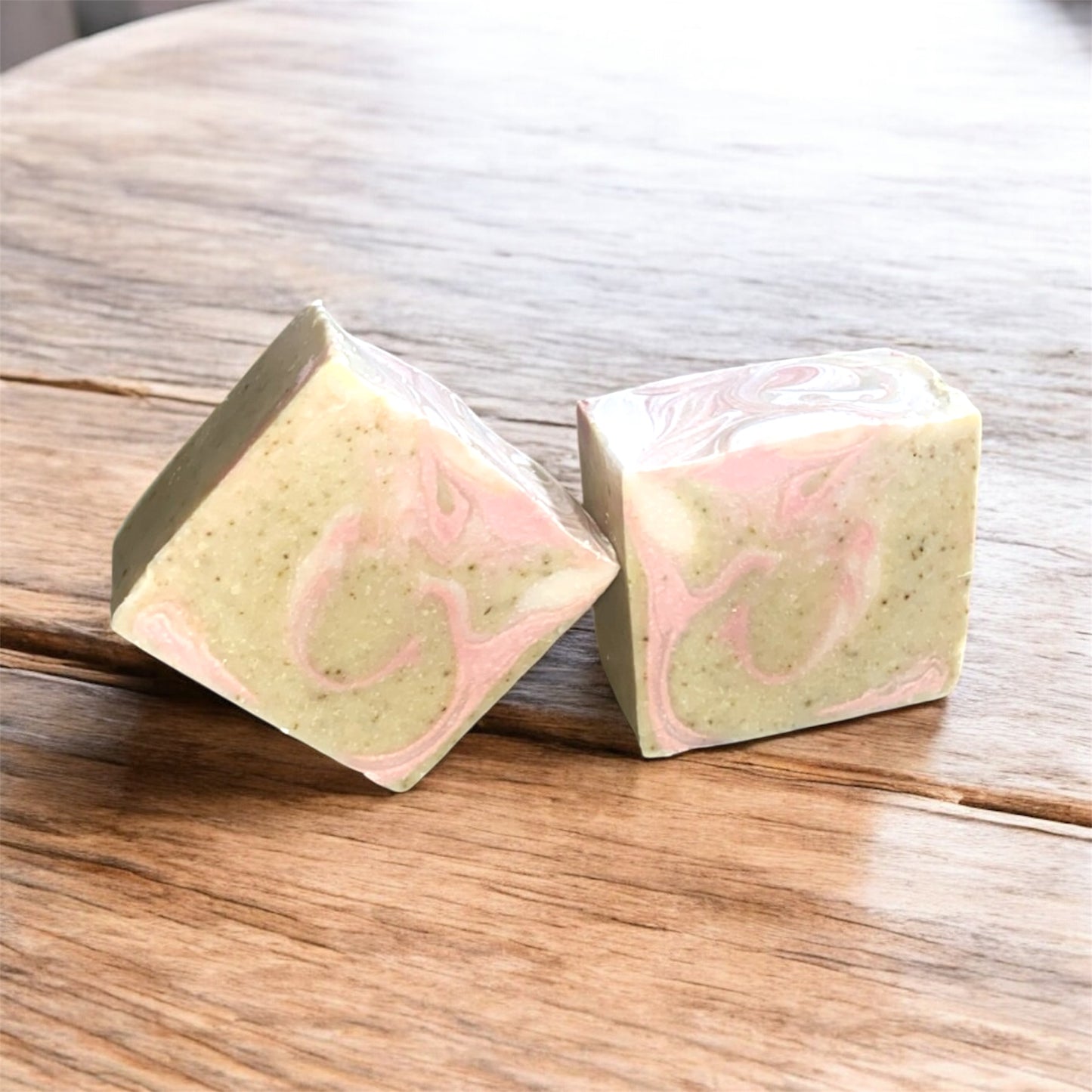 Two square-shaped soap bars with pink and green marbled pattern on a wooden surface