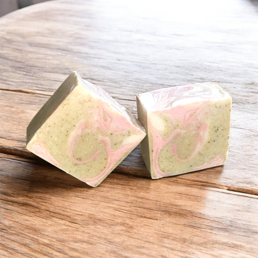 Two square-shaped soap bars with pink and green marbled pattern on a wooden surface