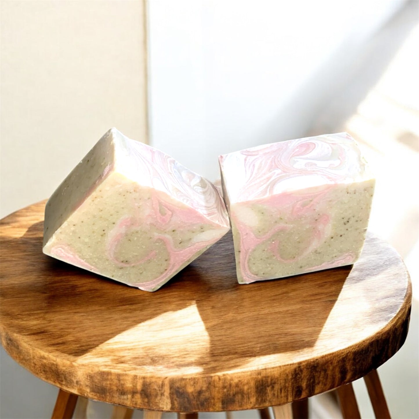 Two pink and white marbled soap bars on a wooden stool with a neutral background
