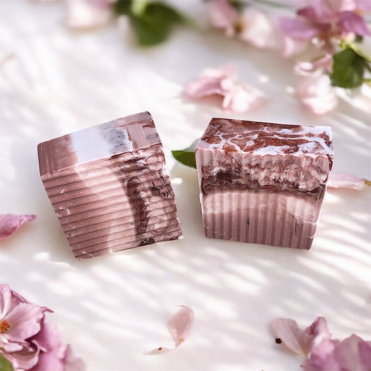 Two marbled soap bars on a light surface with pink flowers in the background