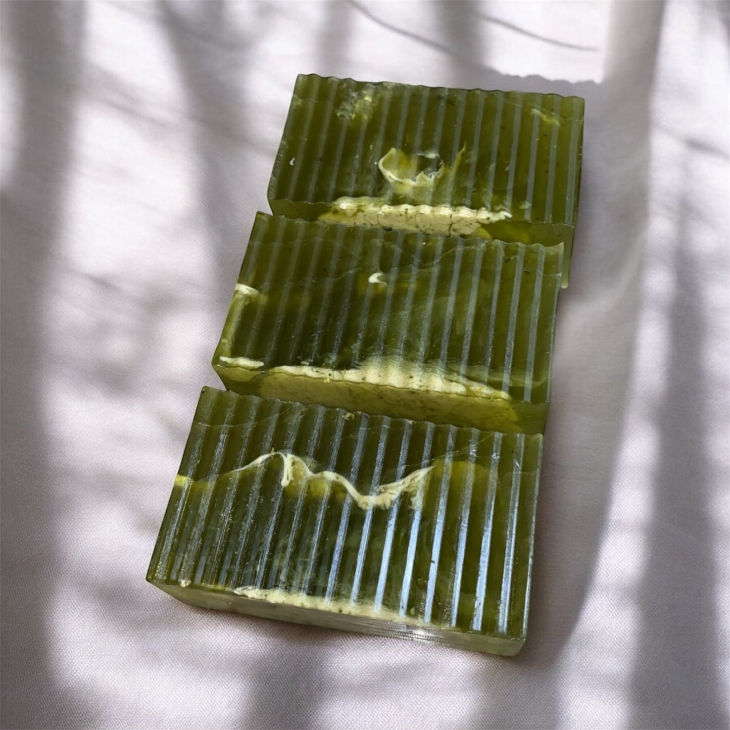 Three rectangular green soap bars with textured surface on a white fabric background