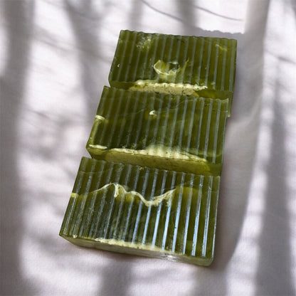 Three rectangular green soap bars with textured surface on a white fabric background