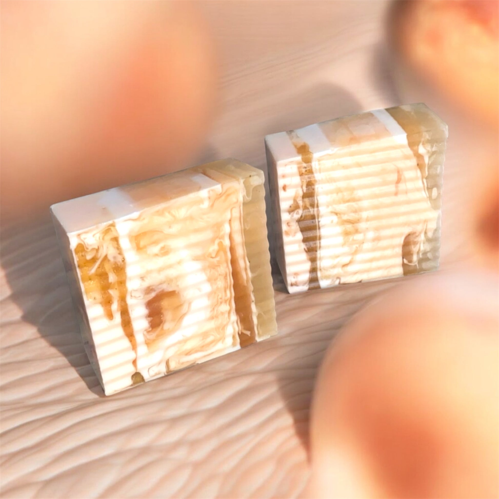 Two stacked soap blocks on a wooden surface with a blurred peach background