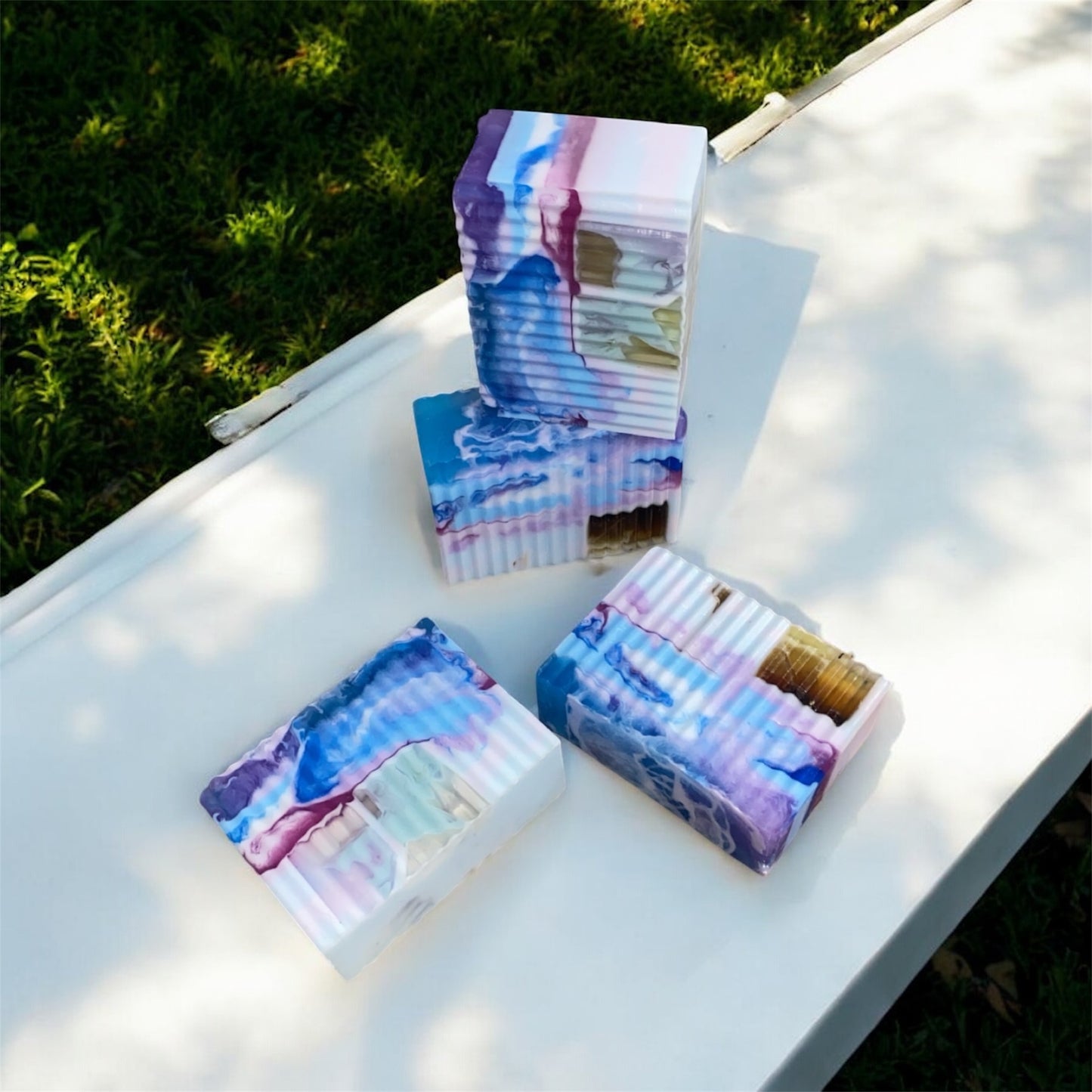 Colorful soap bars on a white surface with grass in the background