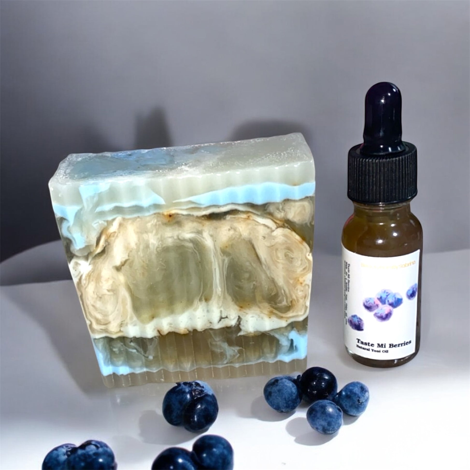 Bar of soap with blueberries and a bottle of yoni  oil on a gray background