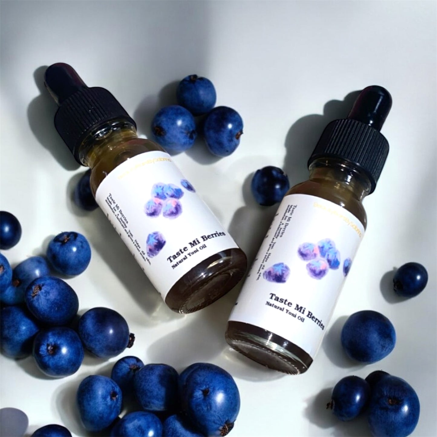 Two bottles of 'Taste Mi Berries' natural blueberry oil with blueberries on a white background