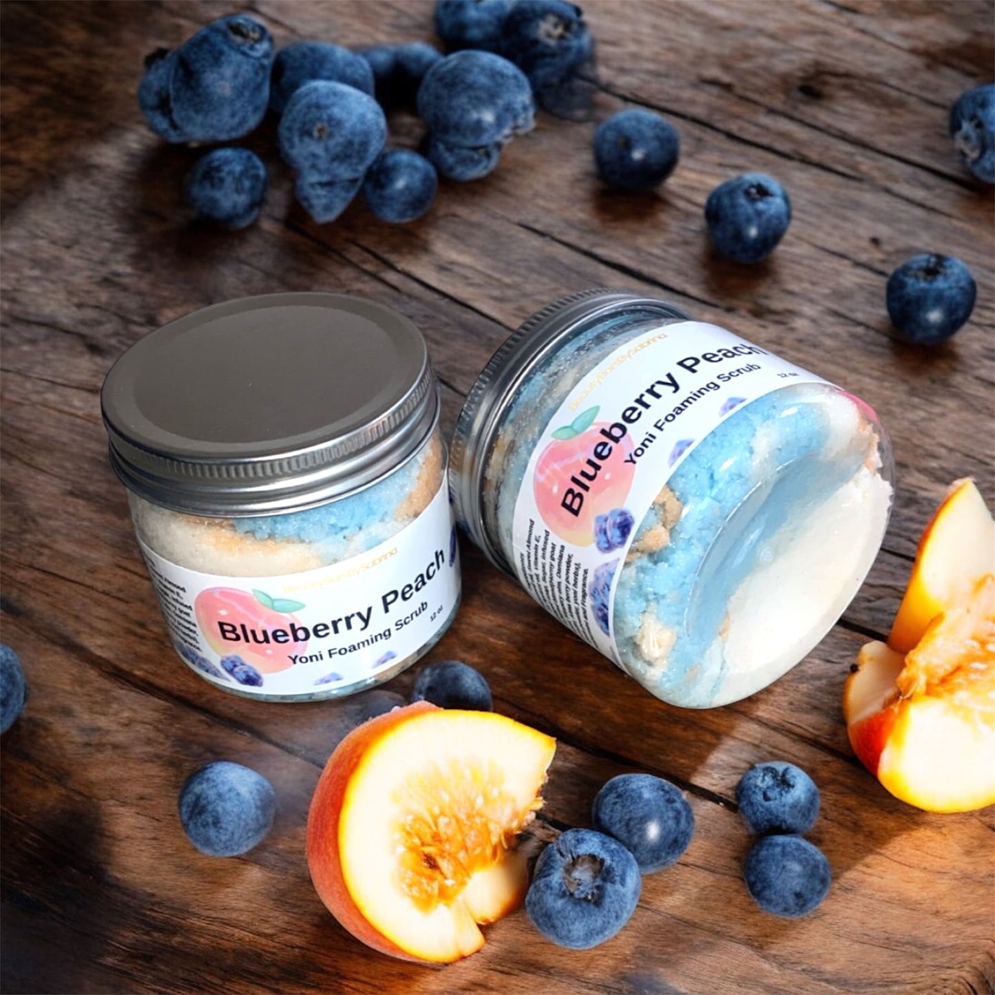Two jars of 'Blueberry Peach' yoni scrub on a wooden surface with blueberries and peaches.