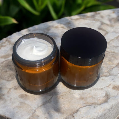 Two brown jars with black lids on a stone surface with cream inside them