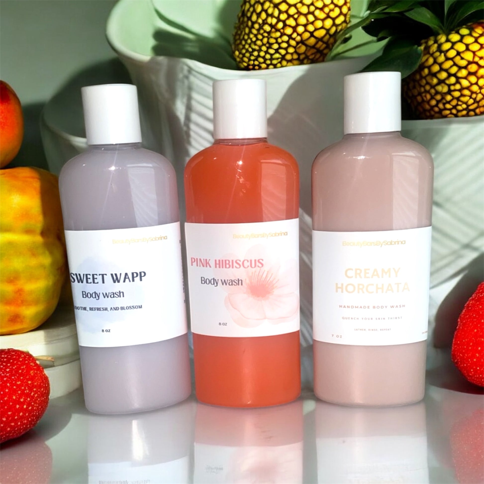 Three bottles of body wash with labels in front of decorative fruits and plants.