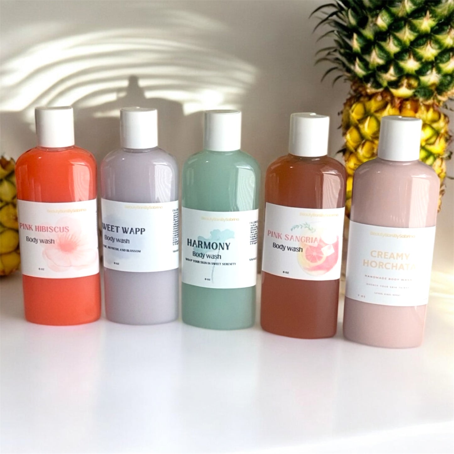 Five bottles of body wash with colorful labels in front of a pineapple.