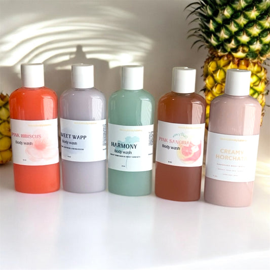Five bottles of body wash with colorful labels in front of a pineapple.