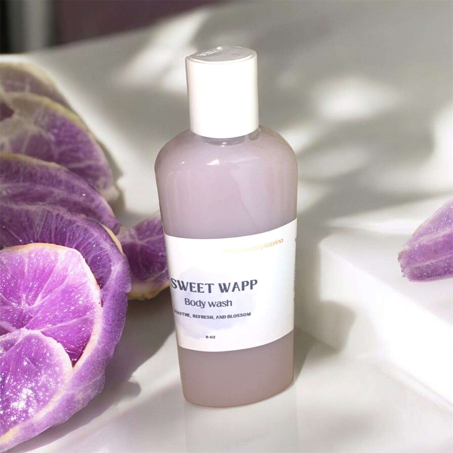 Bottle of Sweet Wapp body wash with purple fruit slices on a light surface